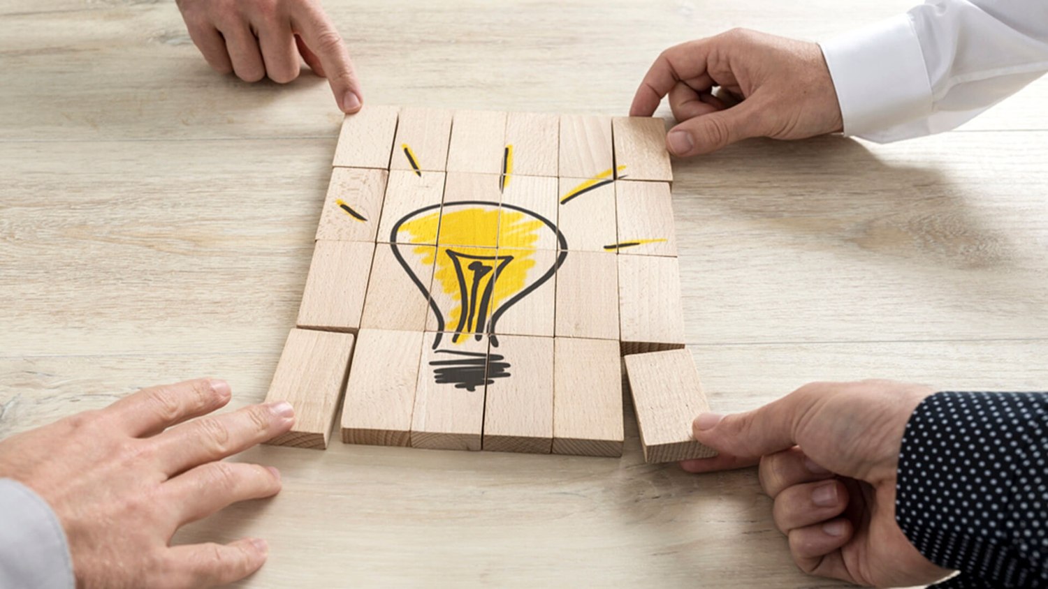 Team members arranging wooden blocks to complete a light bulb illustration.